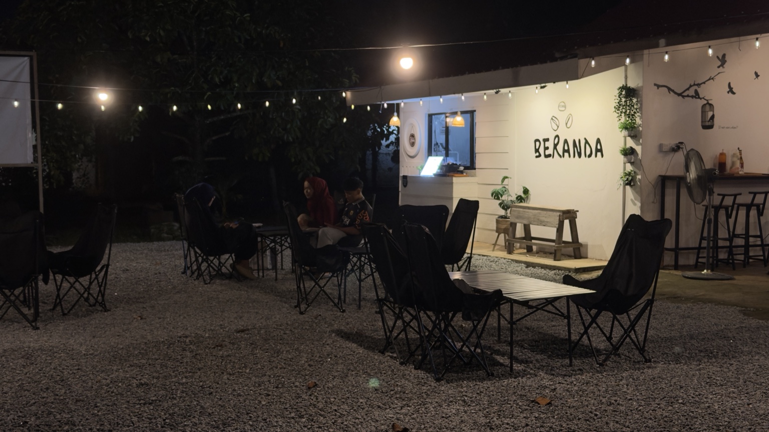 Outdoor seating and warm string lights at Beranda Coffee at night.