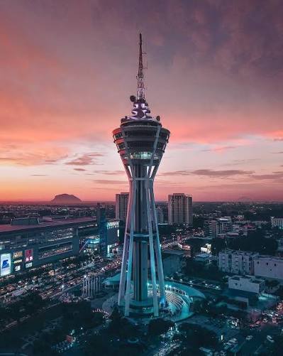 Menara Alor Setar against a pink sunset sky, with city lights below.