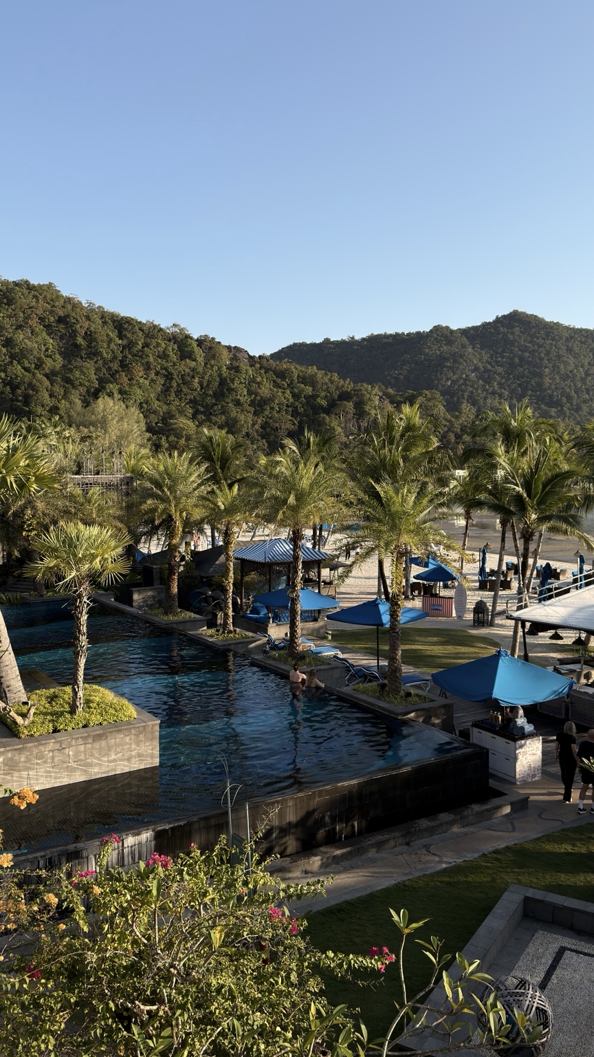 Kolam resort, payung biru dan pokok palma dengan pantai di belakang