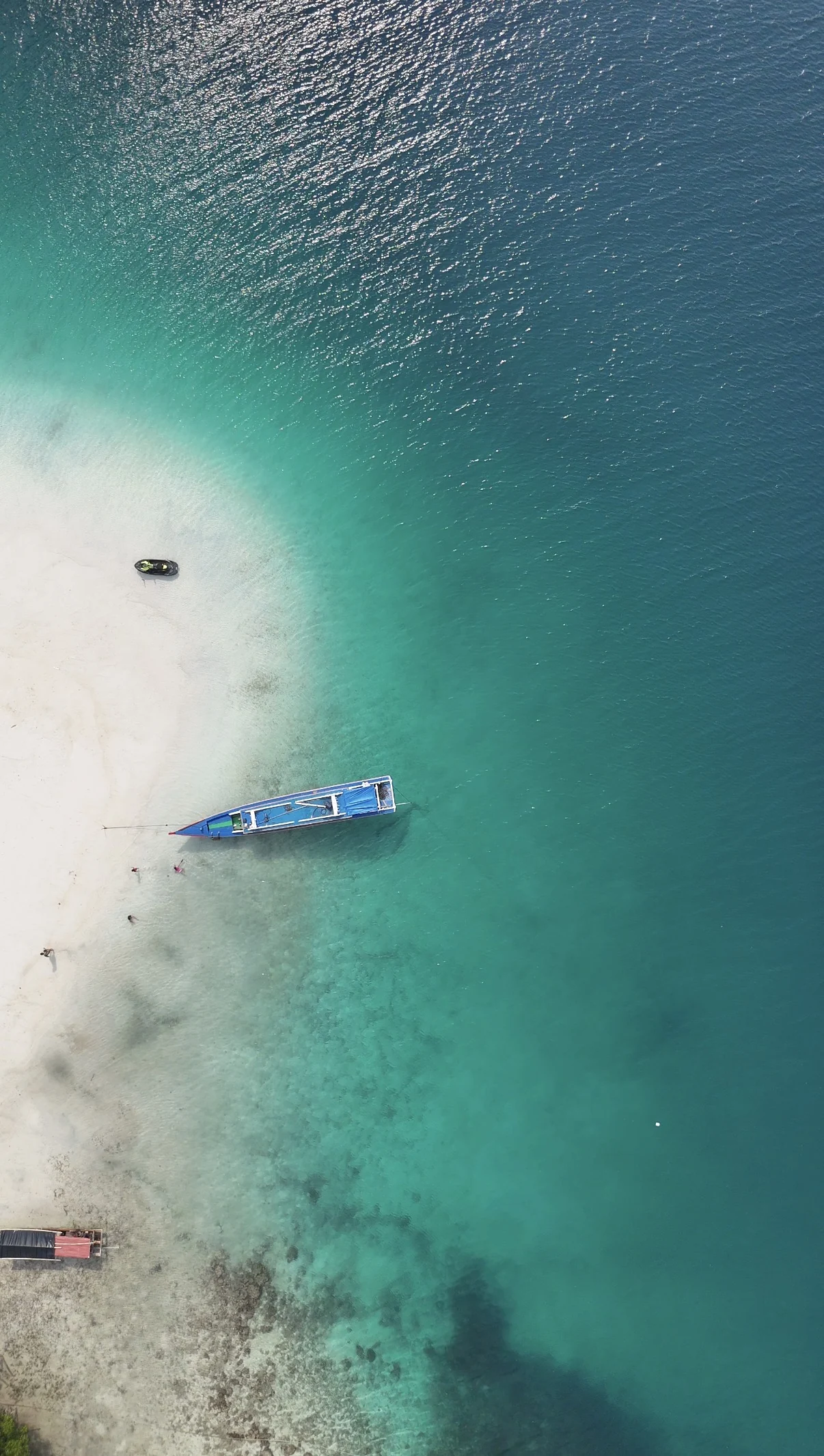 A boat near the shore, with water changing from turquoise to deep blue.