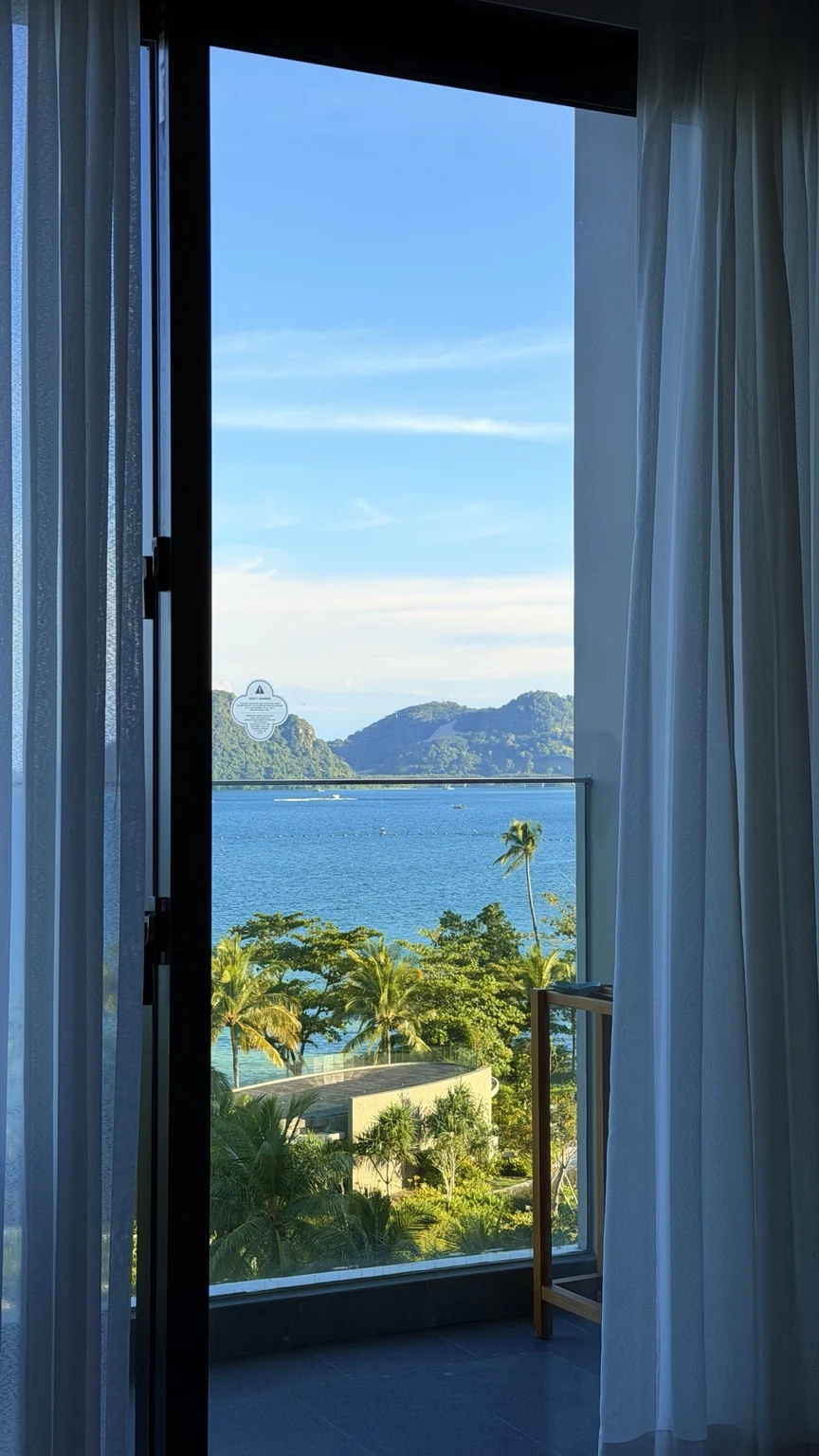 An open balcony doorway framing blue water and coconut palms.