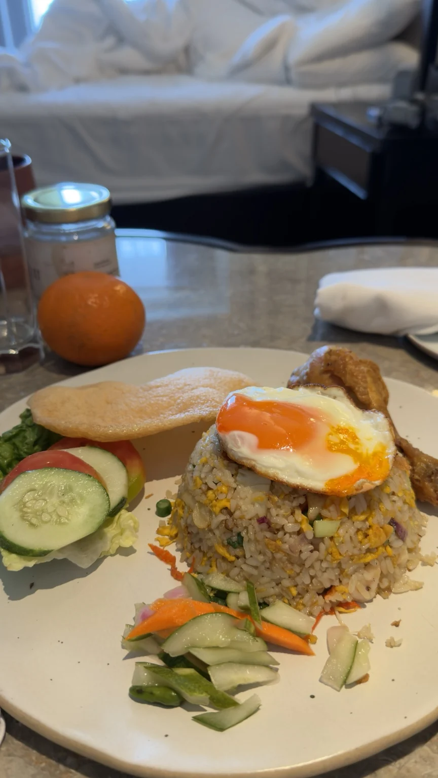 Fried rice topped with a fried egg, crackers and sliced cucumber on a table inside the hotel room.