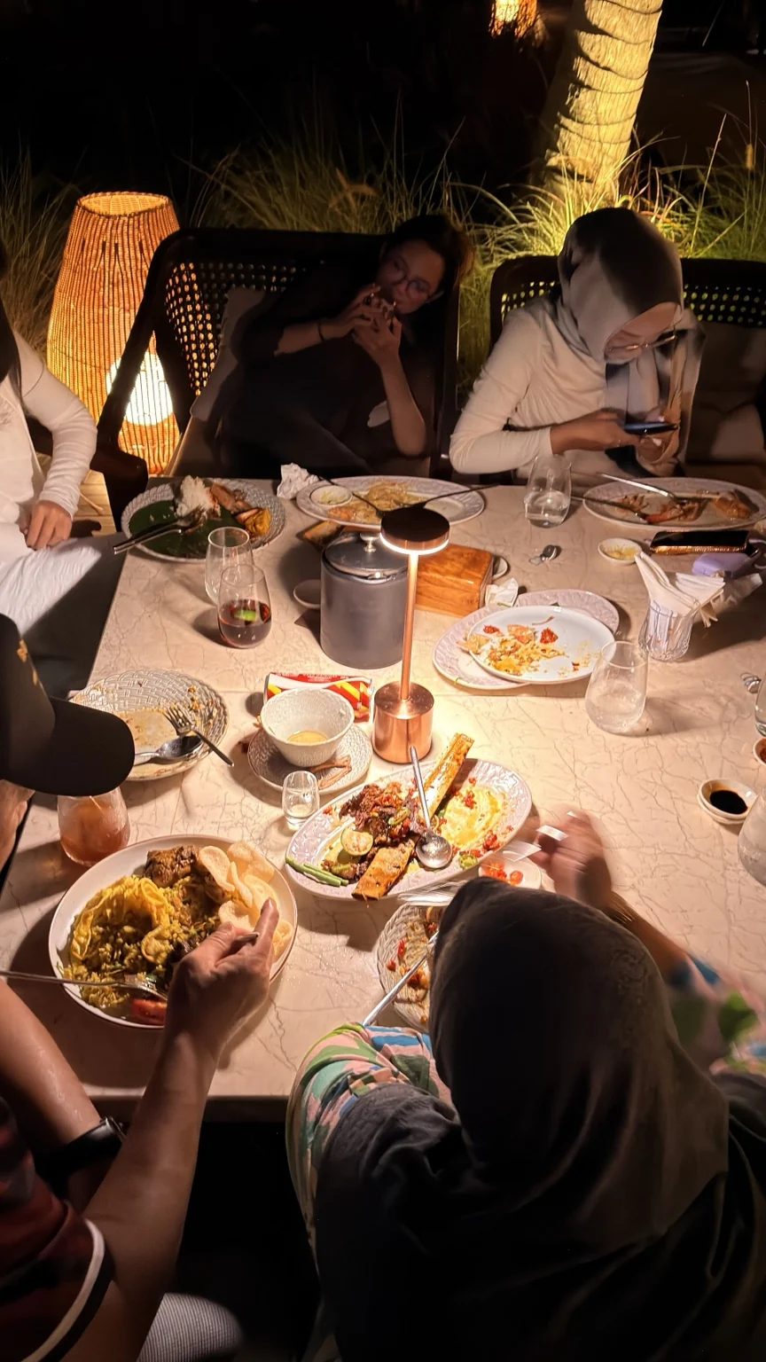 A group of guests dining outdoors under warm evening lighting.
