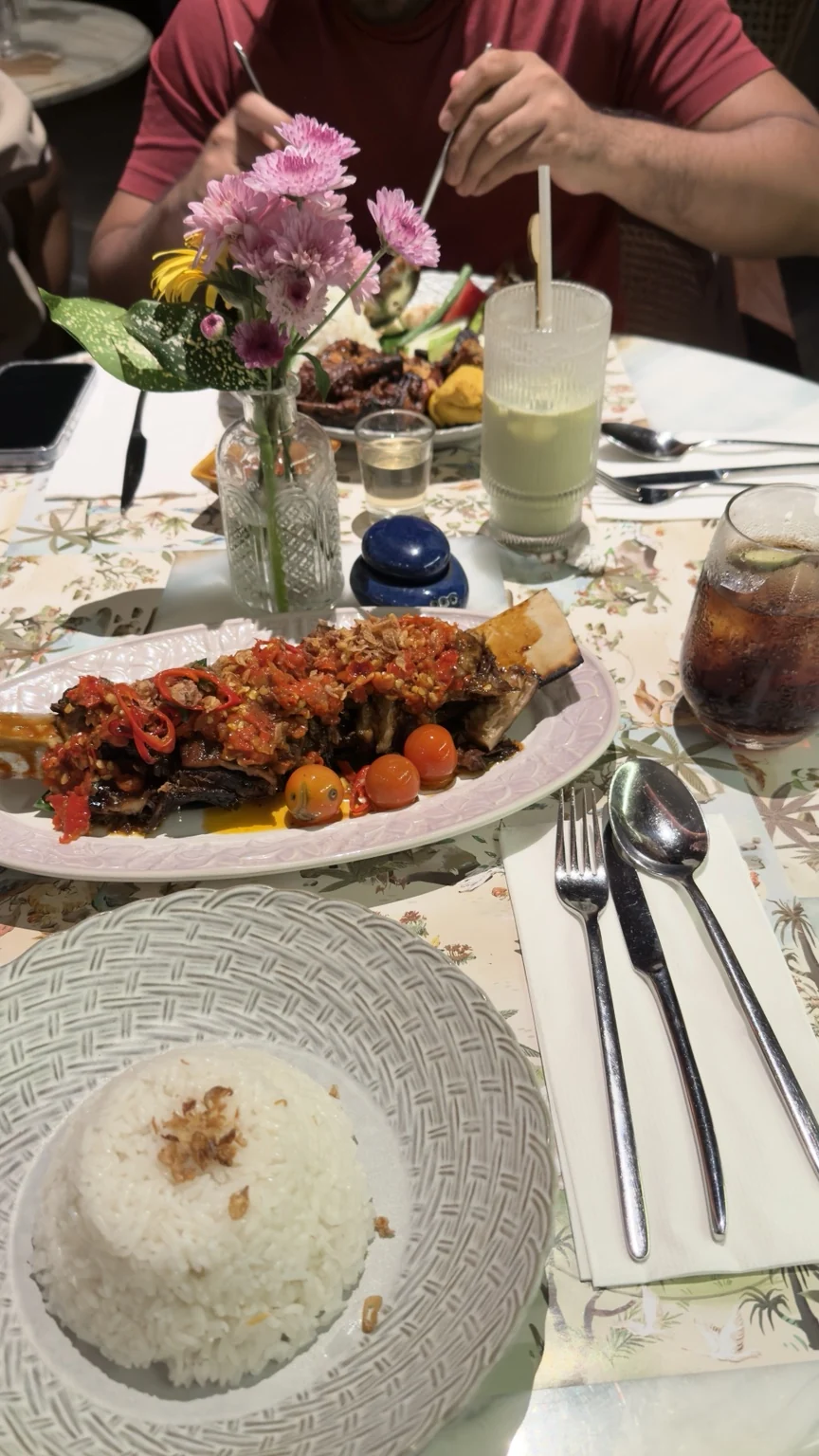 Rice, a shared main dish and drinks on a restaurant table with a flower arrangement.