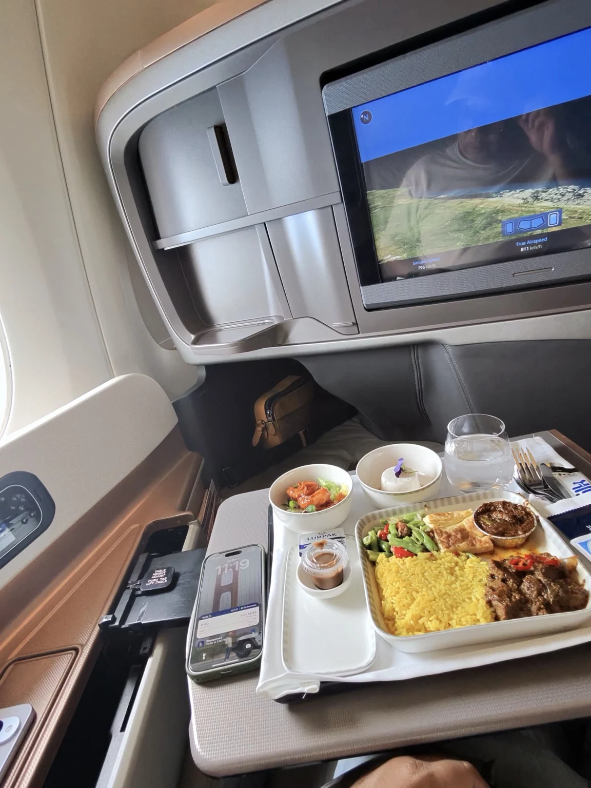 A full meal on a Business Class seat table, with an entertainment screen ahead and a window beside the seat.