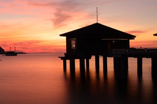 Sunset at TA’AKTANA, a Luxury Collection Resort & Spa, Labuan Bajo, with an overwater pavilion silhouetted against an orange and pink sky.