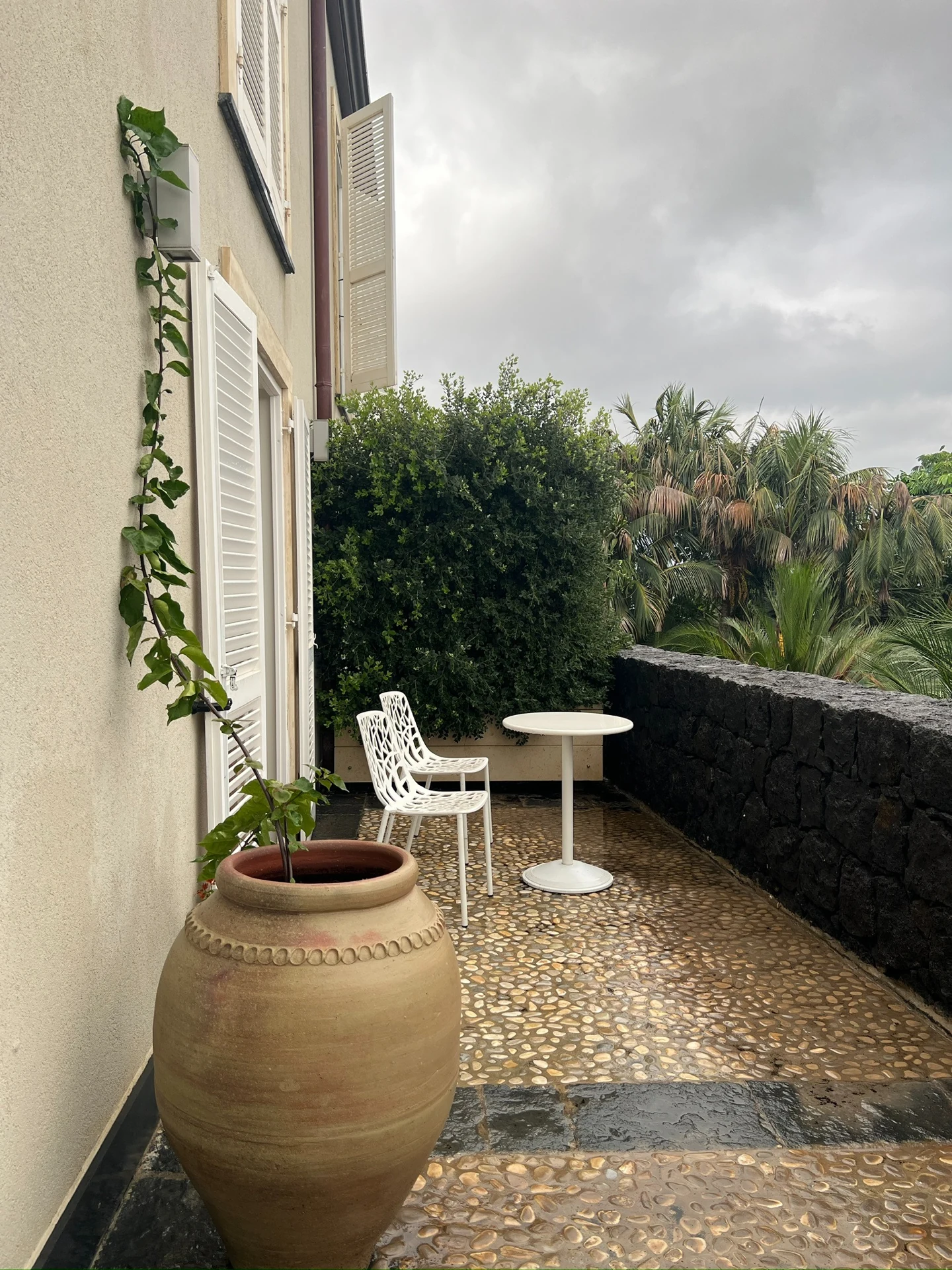 A terrace at Donna Carmela Resort & Lodges with white chairs, a table, and surrounding greenery.