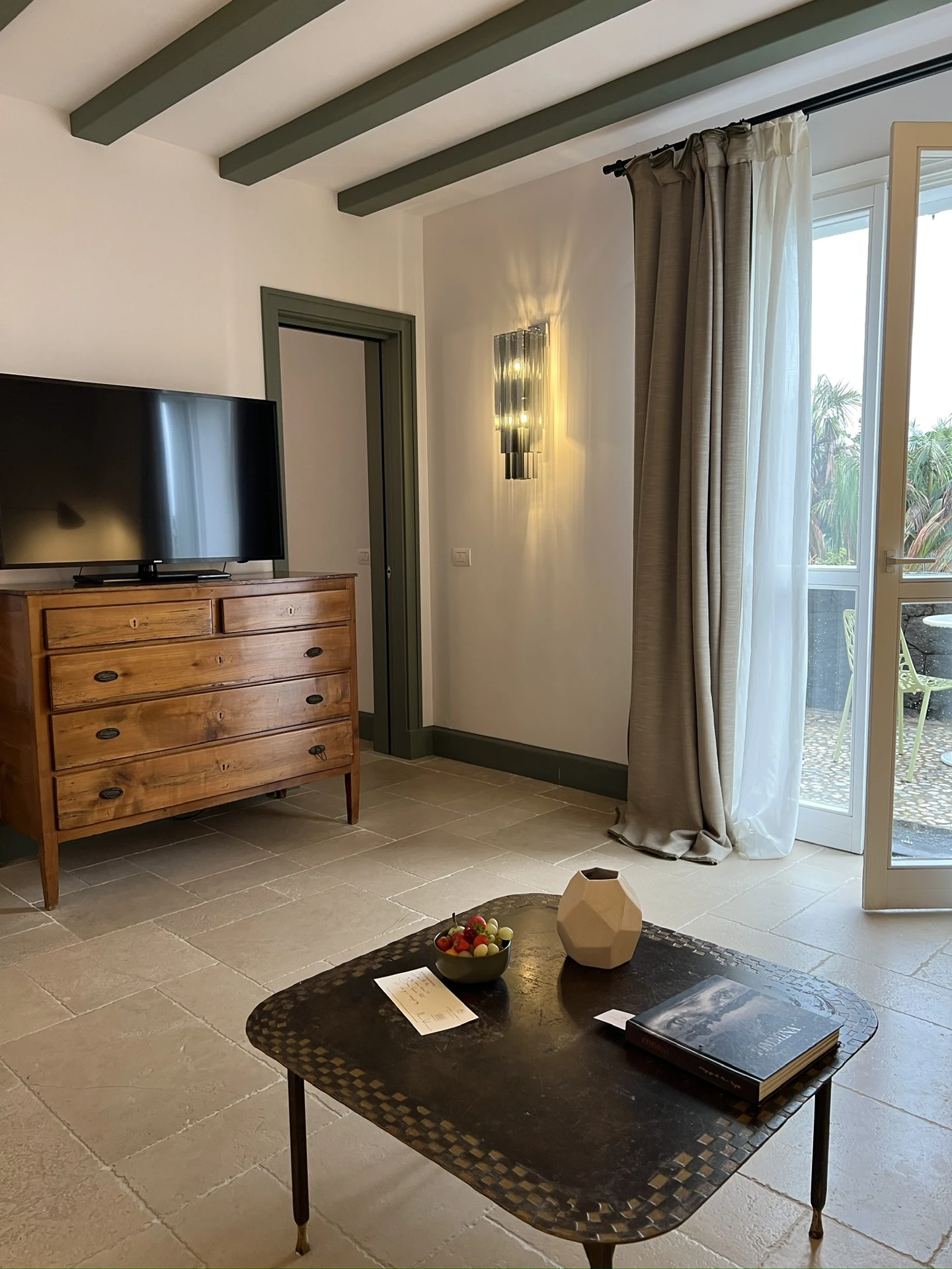An interior at Donna Carmela Resort & Lodges with a wooden dresser and a door opening onto a terrace.
