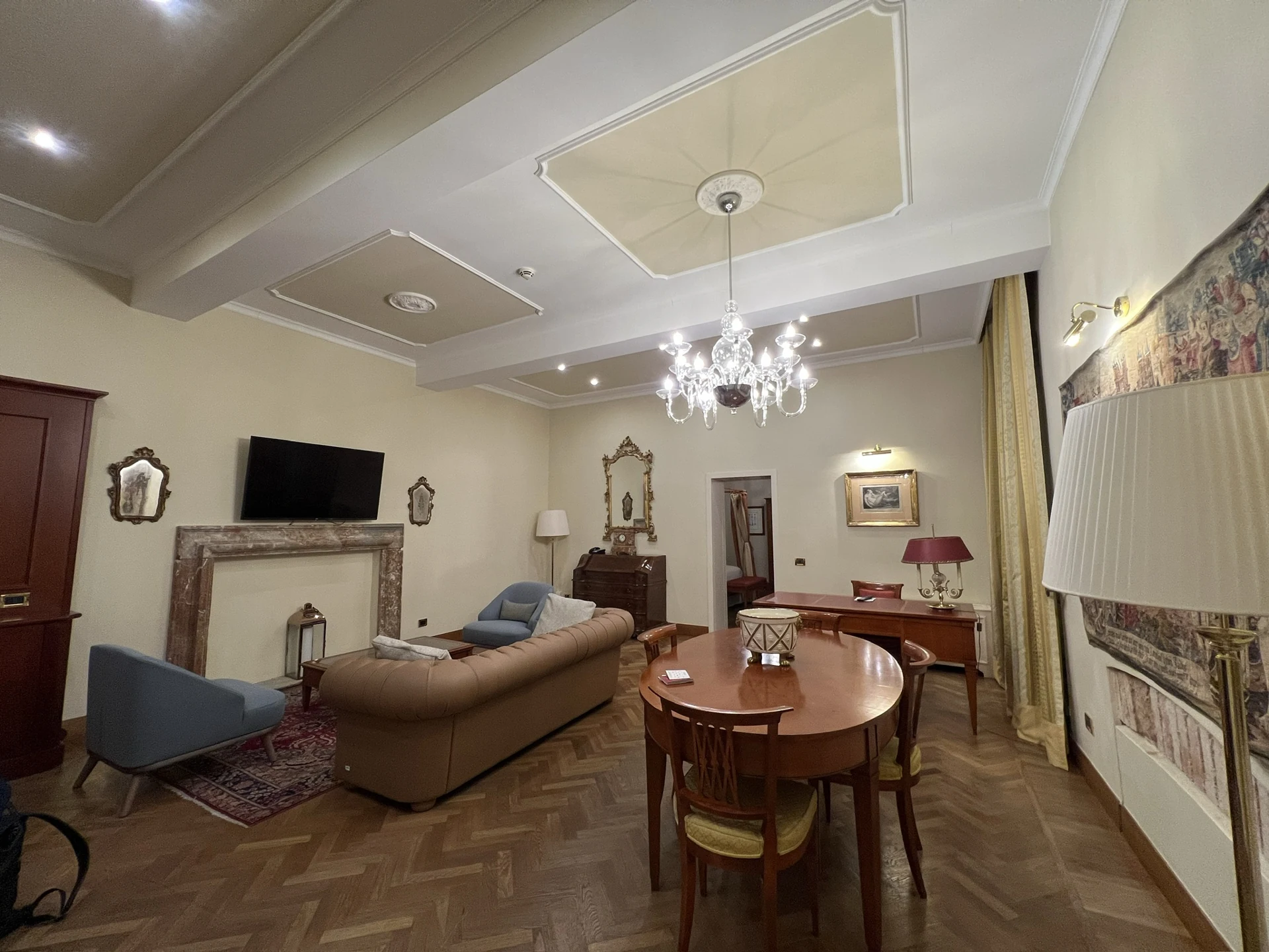 The living and dining room of the Presidential Suite at Villa Toretta, with a chandelier and parquet flooring.