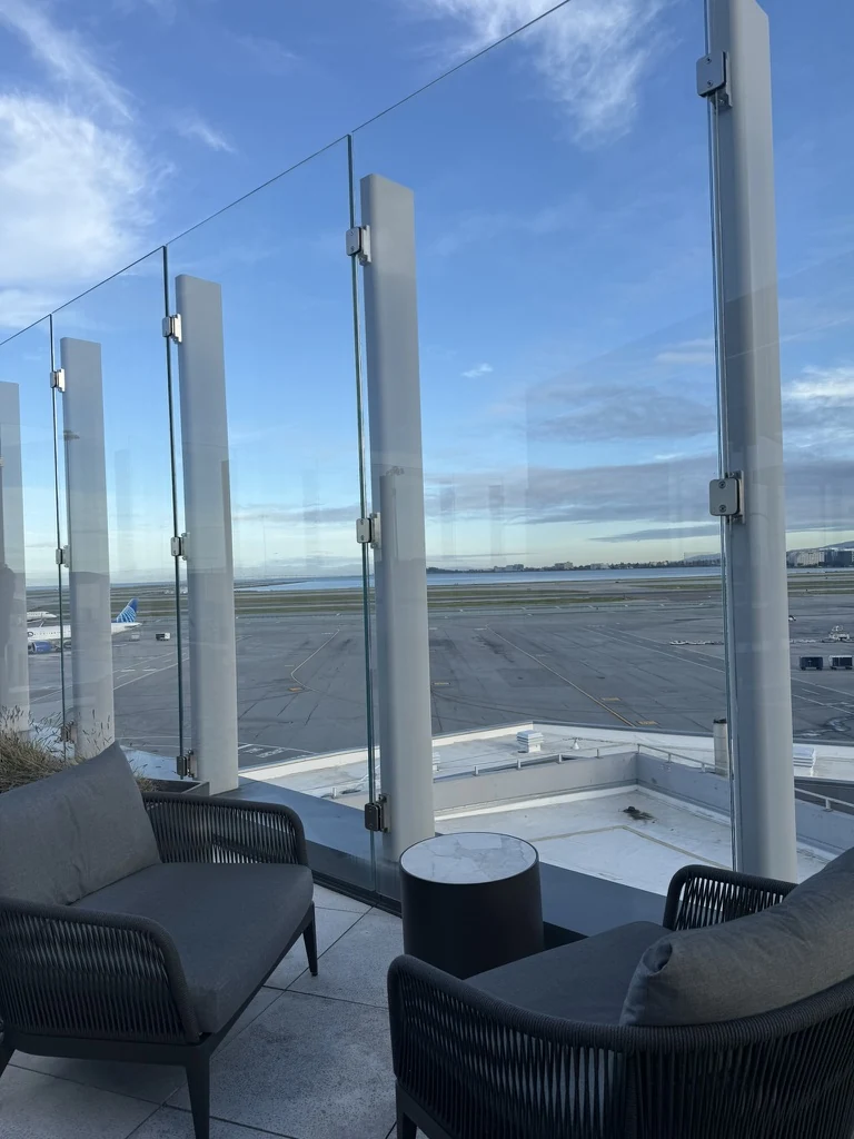 Outdoor seating behind glass wind screens overlooking the airfield at Air Canada’s Maple Leaf Lounge in San Francisco.