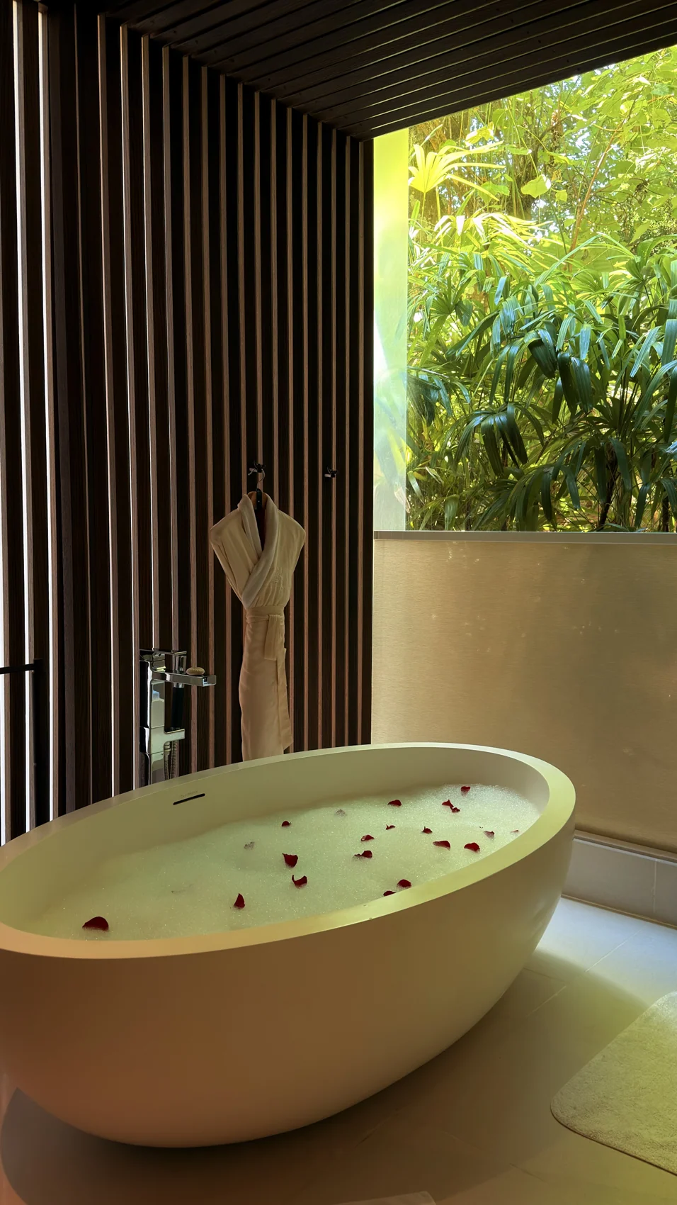 Bathtub berasingan bersebelahan tingkap dan tumbuhan hijau.