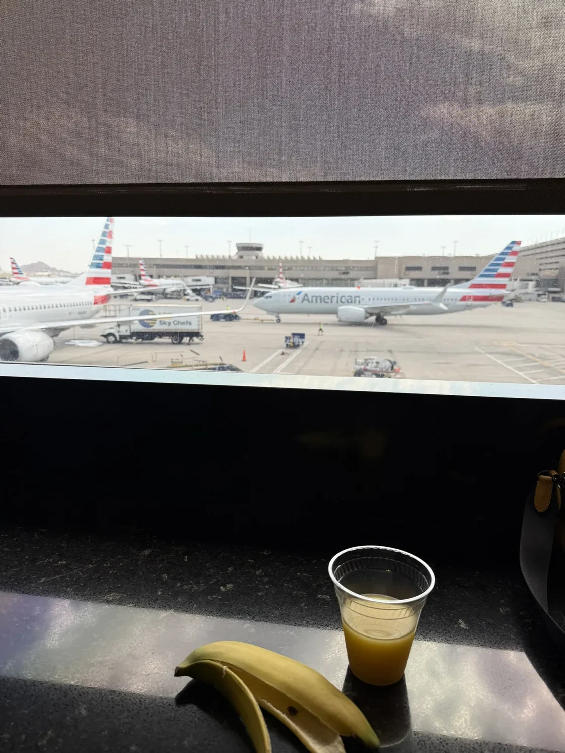 American Airlines aircraft outside a lounge window in Phoenix, with a drink on the counter.