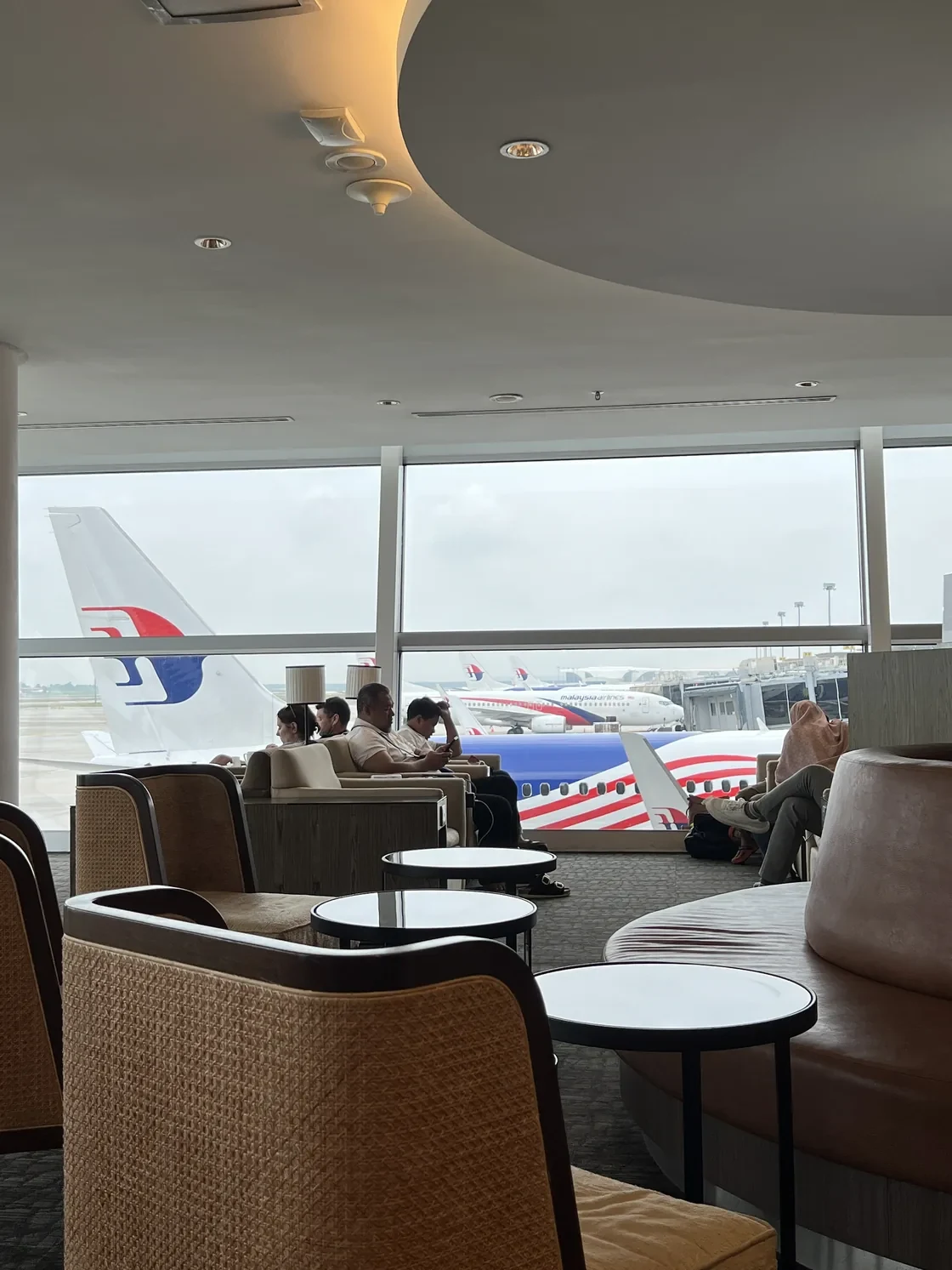 Seats beside large windows overlooking Malaysia Airlines aircraft at the Domestic Golden Lounge.