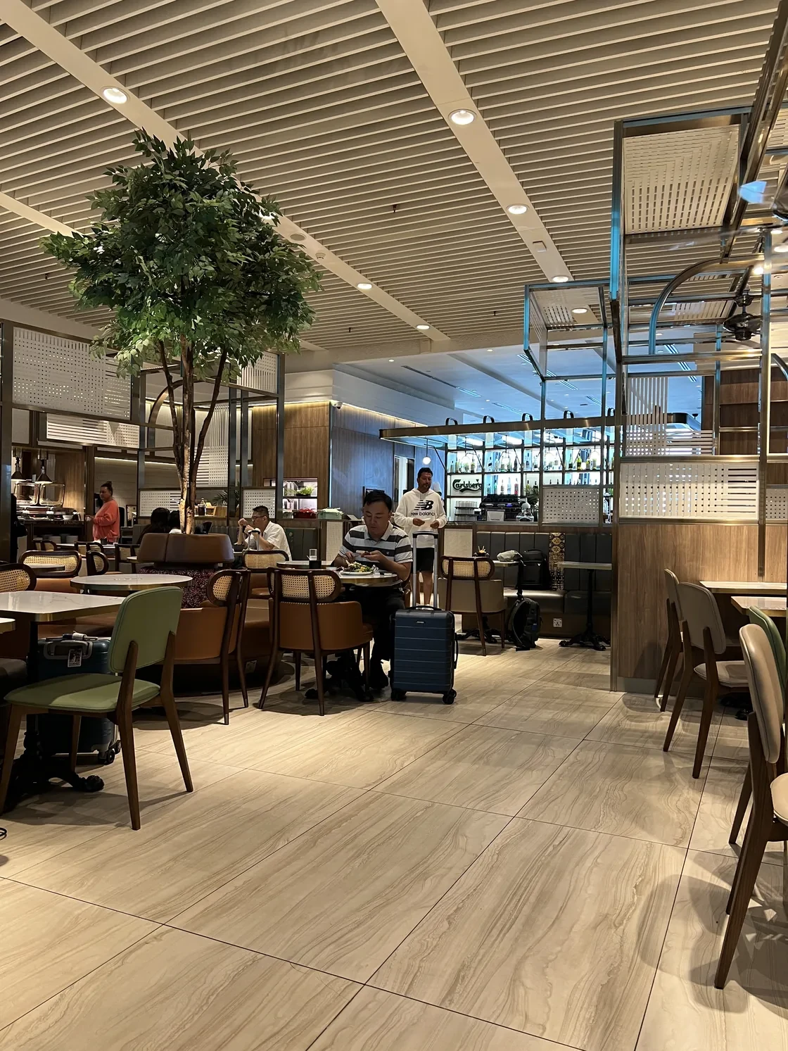Tables and lounge seating around an indoor tree at Plaza Premium KLIA Terminal 1.