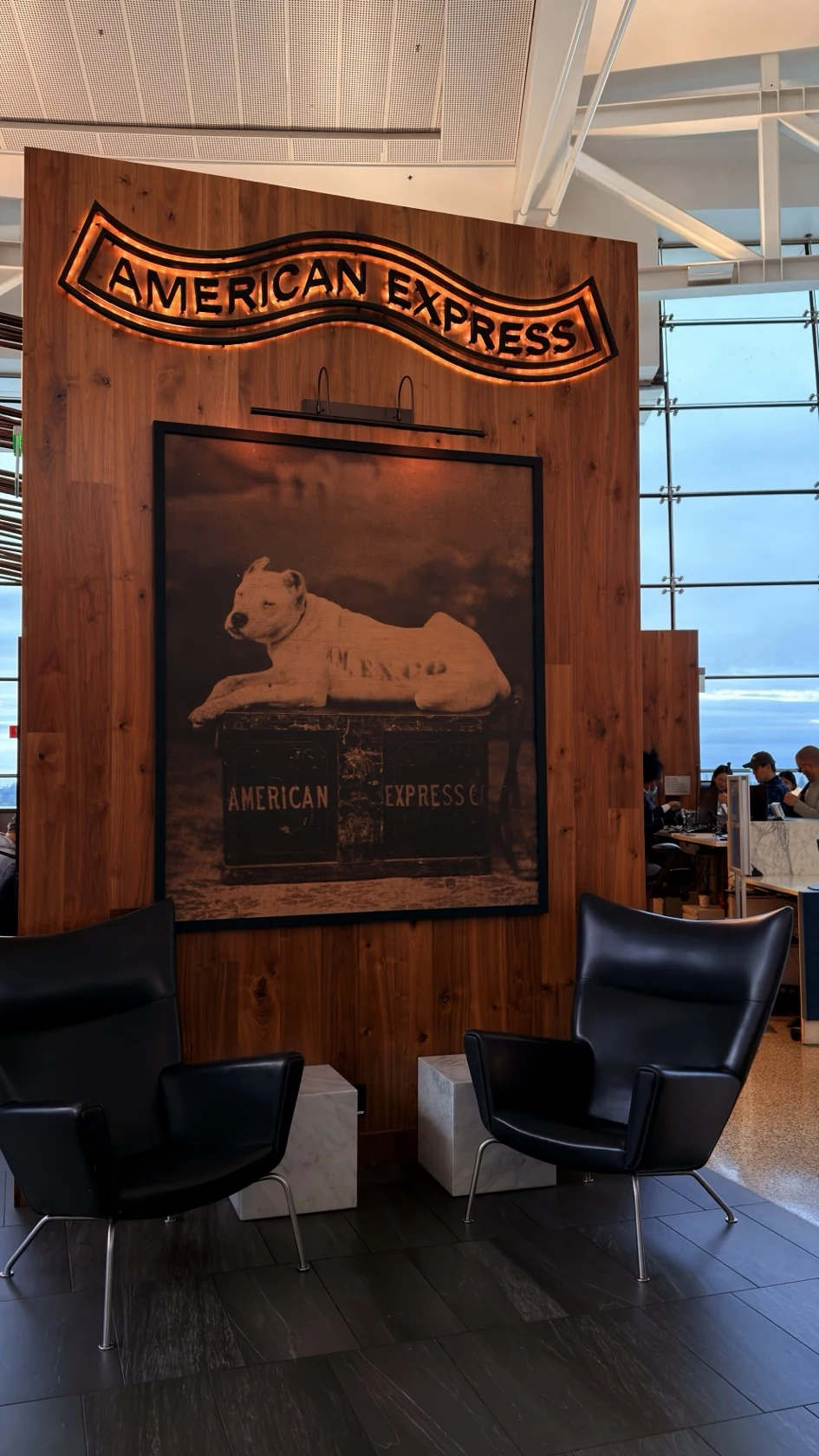 Illuminated American Express sign and a historic dog illustration above two armchairs inside the Centurion Lounge in Seattle.